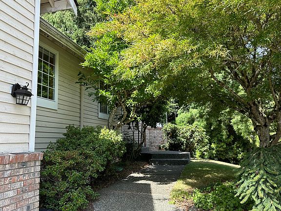 Walkway to the front door lined with beautiful trees, shrubs, and greenery.