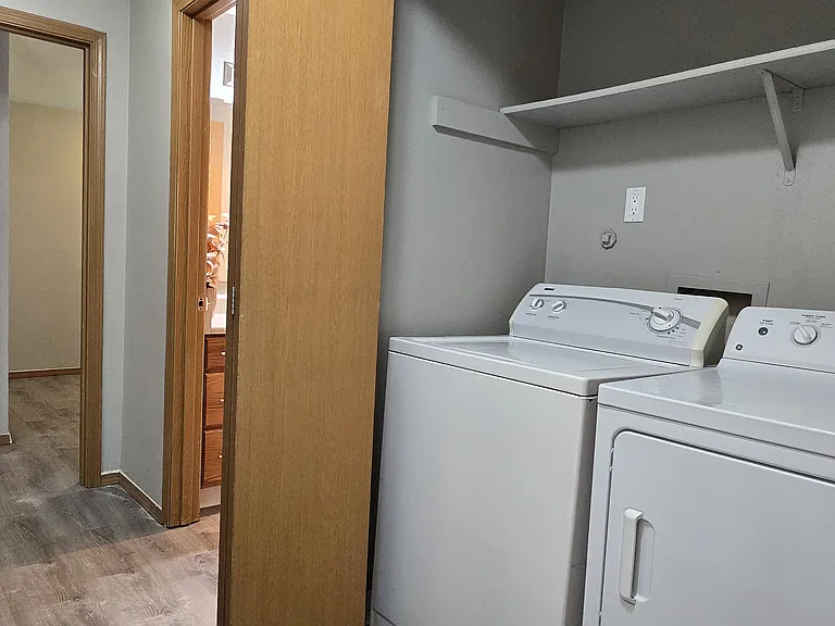 Convenient in-unit laundry area with full-size washer and dryer, plus overhead shelving for extra storage. Located just off the hallway for easy access and everyday functionality.