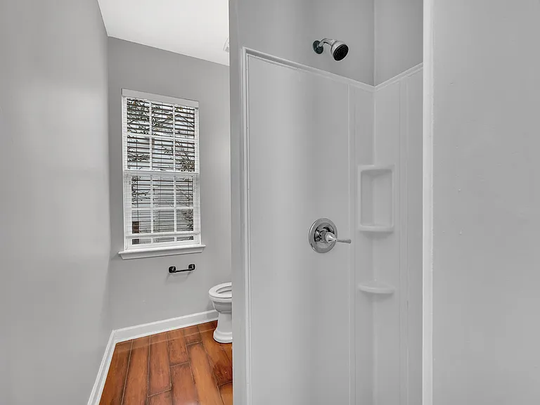 Bathroom with a tub/shower combo, built-in shower shelving, and a window with blinds for light and ventilation.