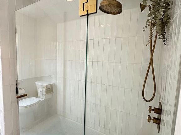 Second level bathroom with unlacquered brass rain shower and bathtub.
