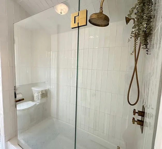 Second level bathroom with unlacquered brass rain shower and bathtub.
