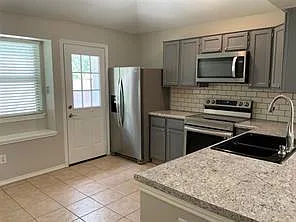 Kitchen featuring gray cabinetry, stainless steel appliances, speckled countertops, a subway tile backsplash, and tile flooring