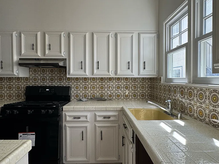 Kitchen under natural light - tile countertops, patterned backsplash, and new range/oven.