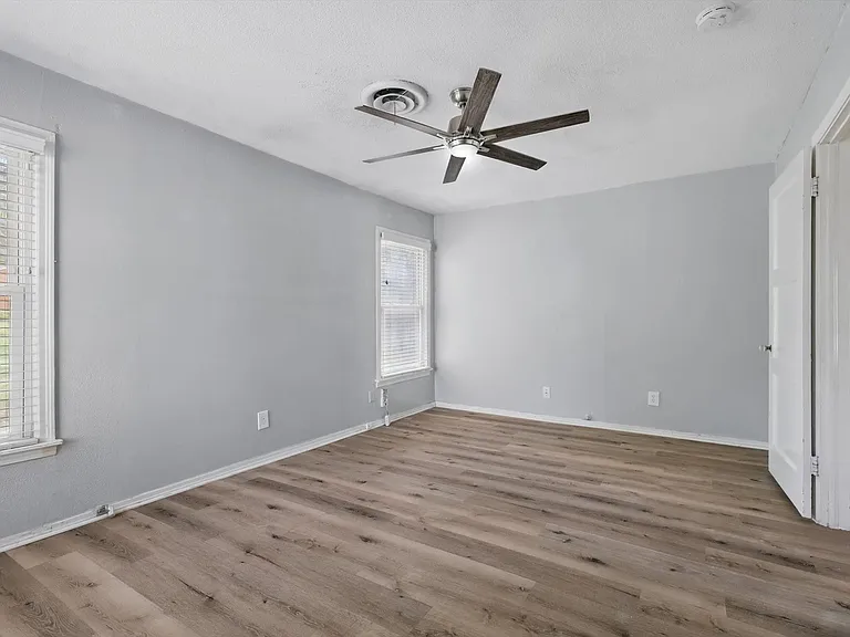 Large primary bedroom featuring neutral soft grey paint, LVP flooring, ceiling fan, closet and multiple windows providing beautiful natural light.
