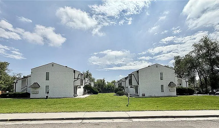 Charming residential complex featuring picturesque white buildings with distinct architectural design, surrounded by lush green lawns under a bright, sunny sky.