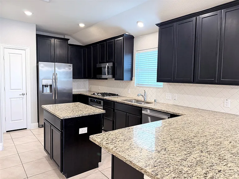 This modern, sun-filled kitchen features elegant espresso cabinetry accented with stylish brushed nickel hardware, complemented by durable granite countertops, a spacious center island with built-in seating, and premium finishes throughout the space.