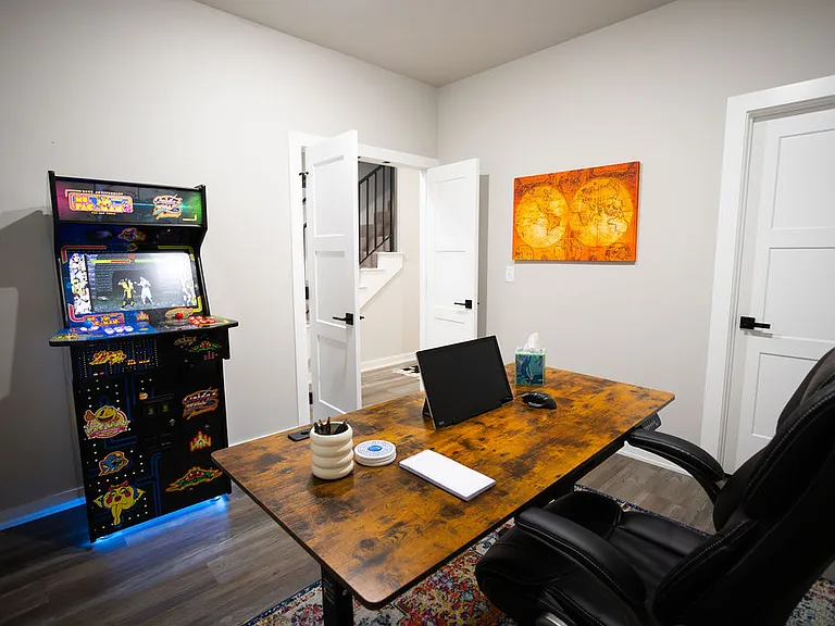 Office area with an adjustable desk for work and an arcade game for play. There is also a large storage closet.