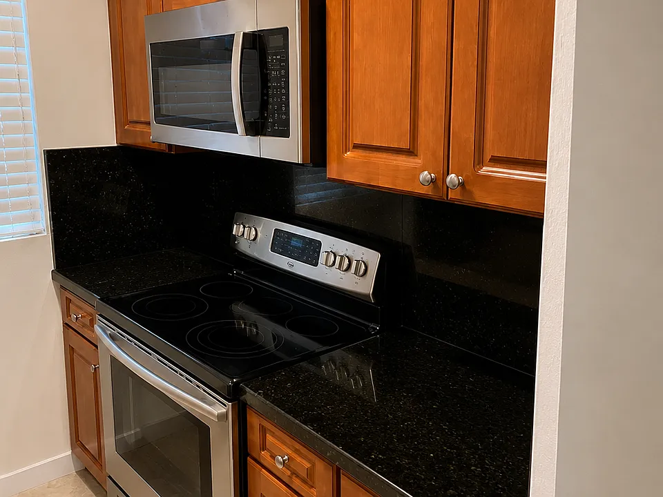 Functional Kitchen featuring warm wood cabinets, stainless steel appliances,black counter tops, ample cabinet space, and a window for natural light