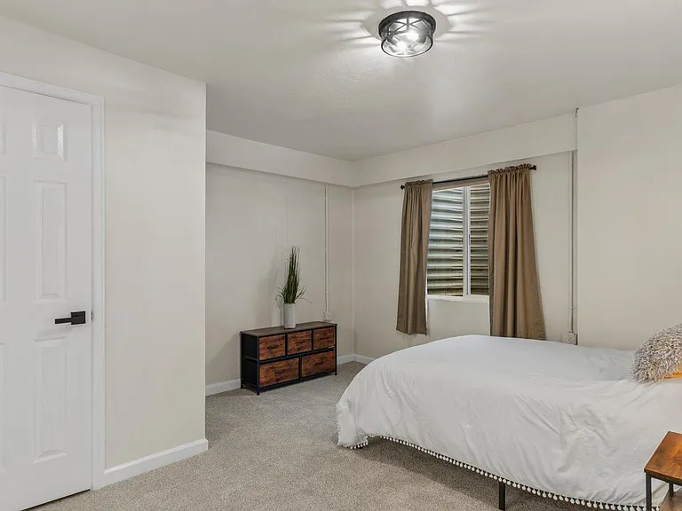 Spacious bedroom with carpeted floors, a large window with curtains, and room for a full/queen bed plus a dresser.