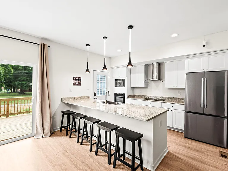 Open kitchen with large granite island seating, stainless appliances, ample cabinetry, and sliding door to the deck.