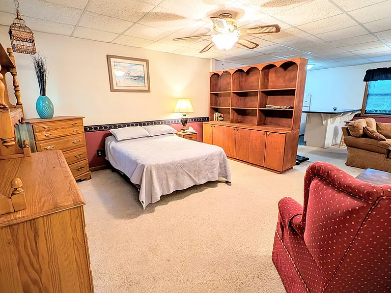 Furnished bedroom suite with full bed, dresser storage, and built-in shelving, plus a sitting area and nearby bar counter.
