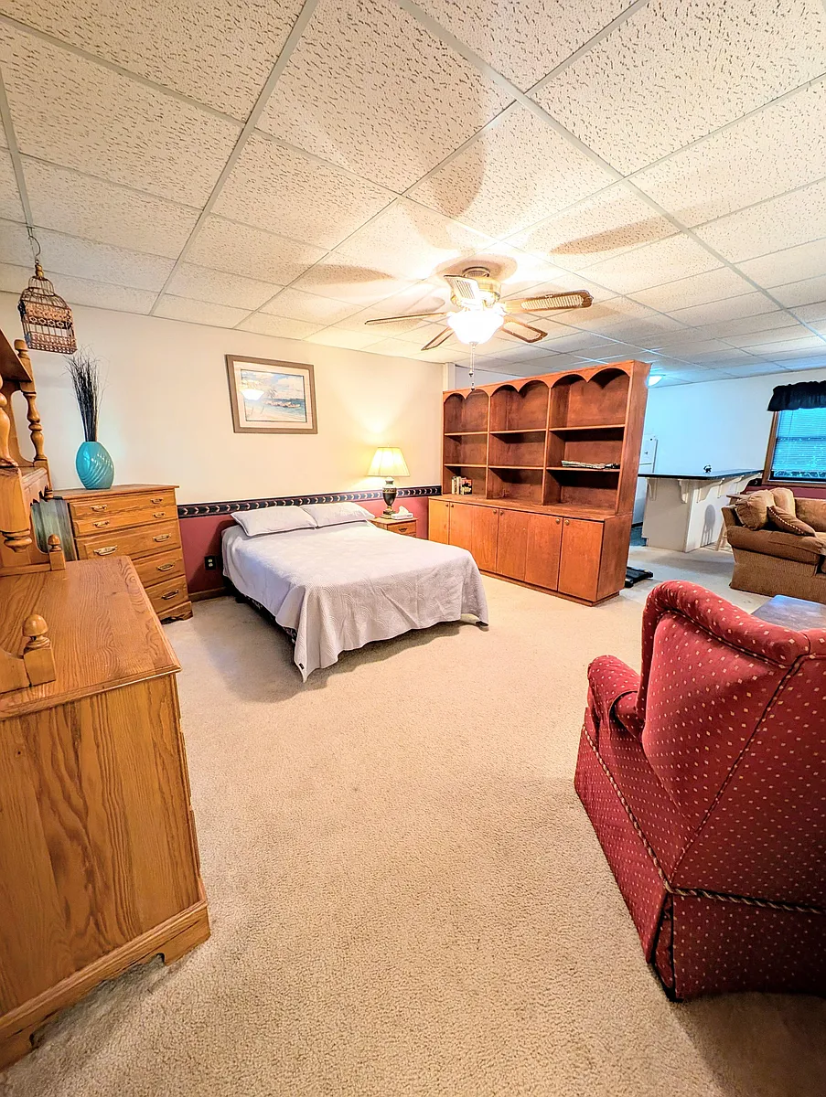 Furnished bedroom suite with full bed, dresser storage, and built-in shelving, plus a sitting area and nearby bar counter. - San Andra Dr