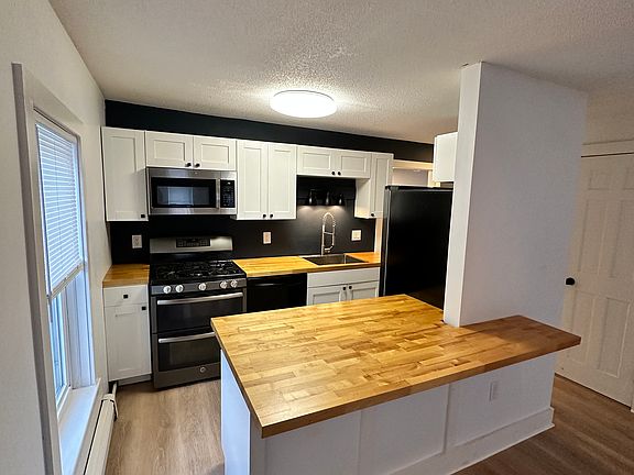 Bar countertop for seating, gas stove, refrigerator, dishwasher and microwave. Kitchen looks into the living room space.