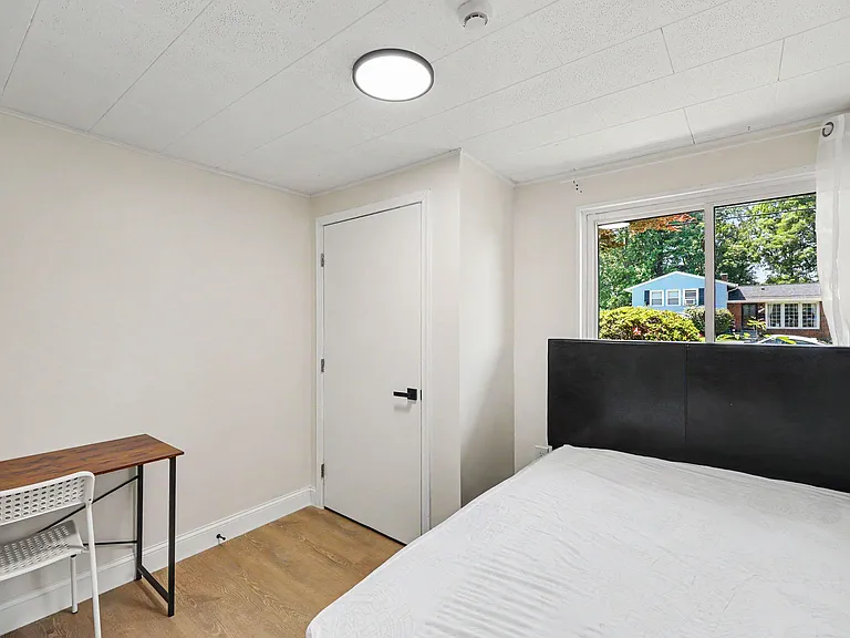 Private bedroom with a large window, wood-style flooring, and space for a bed plus a small work desk.