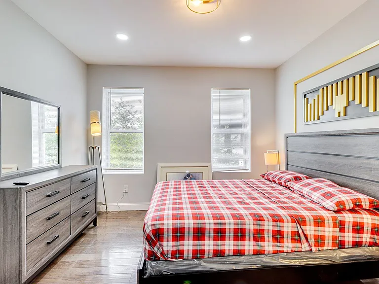 Spacious bedroom with a full bed set, dresser with mirror, and dual windows with blinds for privacy and natural light.