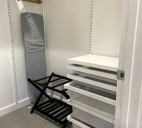 Walk-in closet with brand new Elfa closet system, iron and ironing board, portable heater, and hangers.