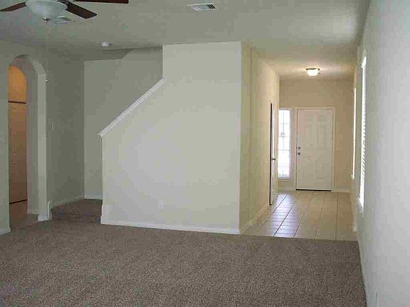 View of your entry from your huge family room, with carpet, ceiling fan with light fixture and stairs leading to the second floor and arch entry into your other bedrooms.