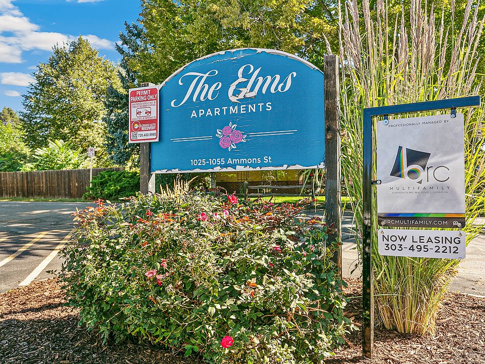 Charming entry sign for The Elms Apartments surrounded by lush greenery and vibrant flowers, located at 1025-1055 Ammons St, offering a welcoming and scenic environment.