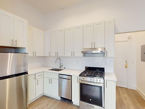 Kitchen with multiple cabinets, refrigerator, stove, range hood, and sink