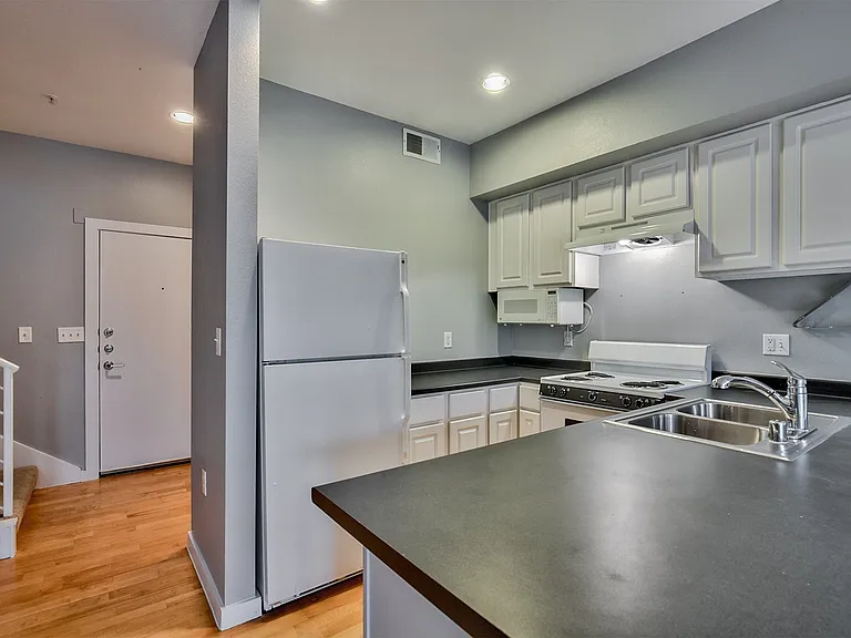 Compact kitchen featuring white cabinetry, dark countertops, a double-basin stainless steel sink with a chrome faucet, and a white electric range with an overhead microwave