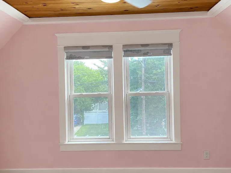 Bright second-floor bedroom featuring two large windows, a ceiling fan, soft carpeting, and a beautiful wood-accent ceiling that adds warmth and character.