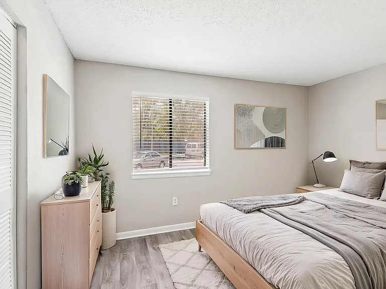 Bright, stylish bedroom with modern decor, featuring large window, cozy bedding, and a sleek dresser with potted plants.