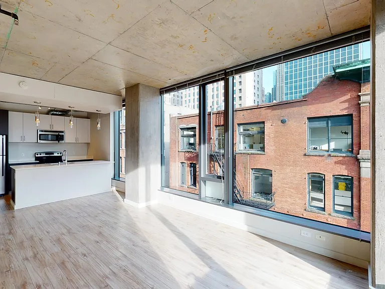 Apartment kitchen with stainless steel appliances, dining and living room with wood-style flooring and floor-to-ceiling windows.