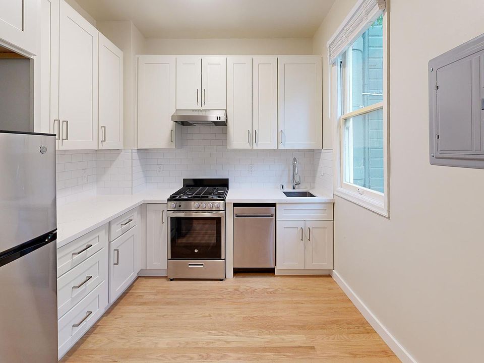 Kitchen with multiple cabinets, refrigerator, stove, range hood, and sink