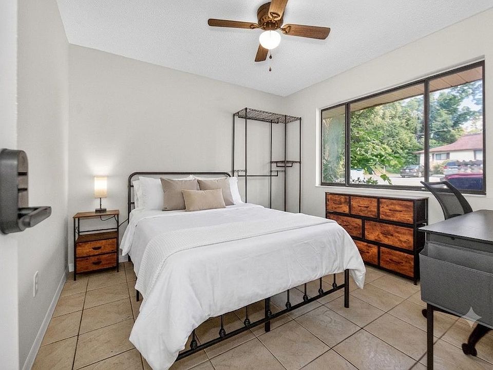 Furnished bedroom with a full bed, dresser, and desk, plus a large window and ceiling fan for everyday comfort.