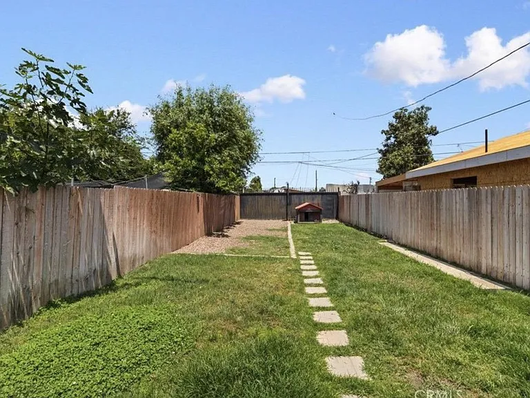 Fenced backyard with a grassy lawn, gravel area, and a stepping-stone pathideal for outdoor lounging or pets.