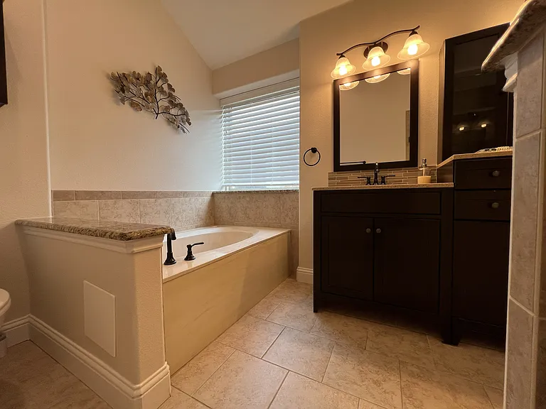 Spa-inspired primary bathroom featuring soaking tub, granite countertops, and walk-in glass shower.