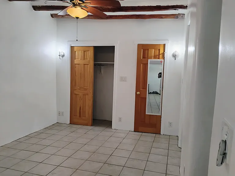 Bedroom with two closets, tile floors and remote fan. Note the original vigas on the ceiling.