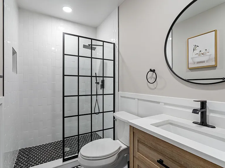 Updated bathroom with a glass-enclosed shower, hex tile flooring, and a single-sink vanity with matte black fixtures.