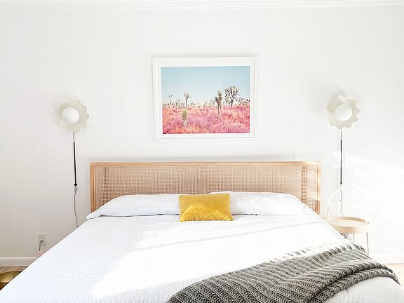 Sun-soaked master bedroom with a king bed, woven cane headboard, blush velvet curtains, and bold graphic rug. Warm, modern, and inviting_designed for comfort with a clean, relaxed vibe.