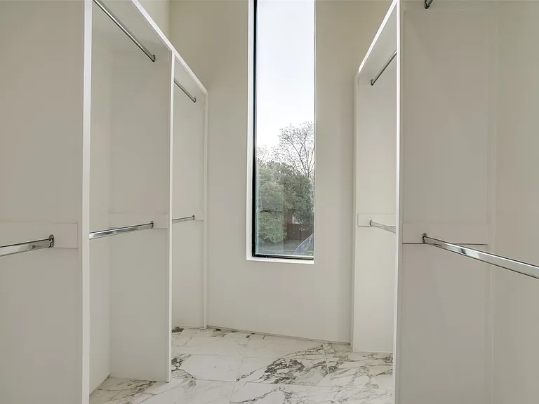 Spacious walk-in closet featuring white built-in shelving, chrome hanging rods, and a tall vertical window