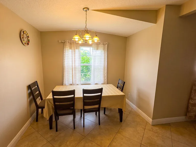 Dedicated dining area with tile flooring, chandelier lighting, and a window with curtainsideal for everyday meals.