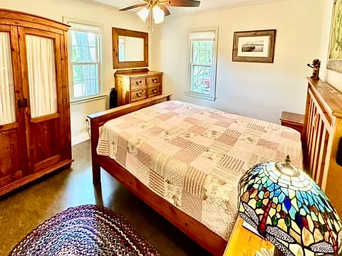 A sunny Queen bedroom with two windows and ceiling fan for air circulation.