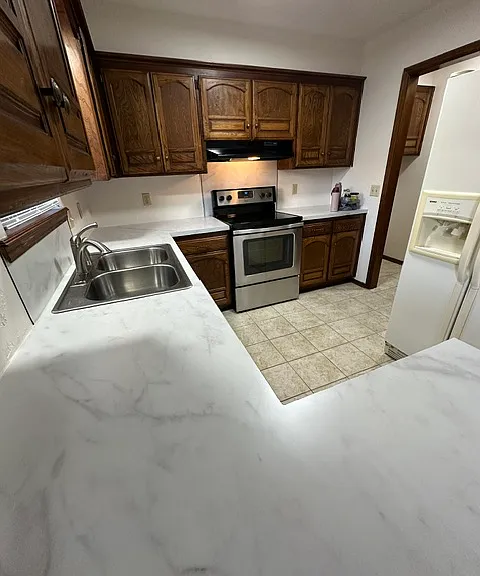 Kitchen with stainless steel dishwasher, stove and sink. Refrigerator with ice and water on the door.