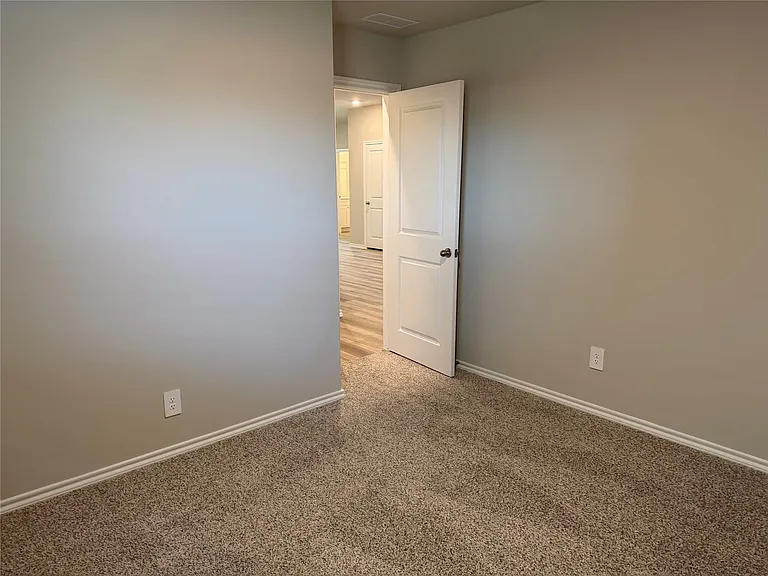 Neutral-toned room featuring plush carpet flooring, white baseboards, and a solid core interior door with a dark knob