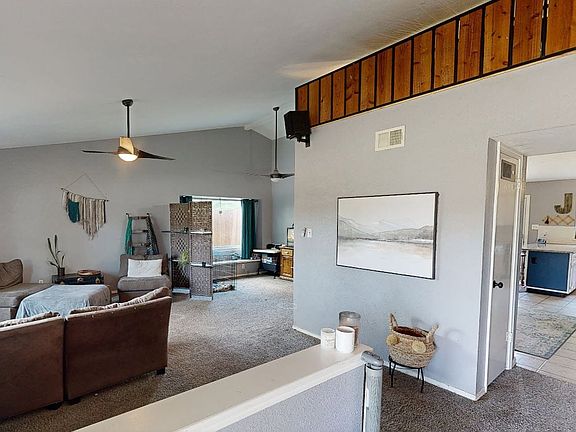 Spacious living area featuring vaulted ceilings with ceiling fans, carpeted flooring, and ample natural light from multiple windows
