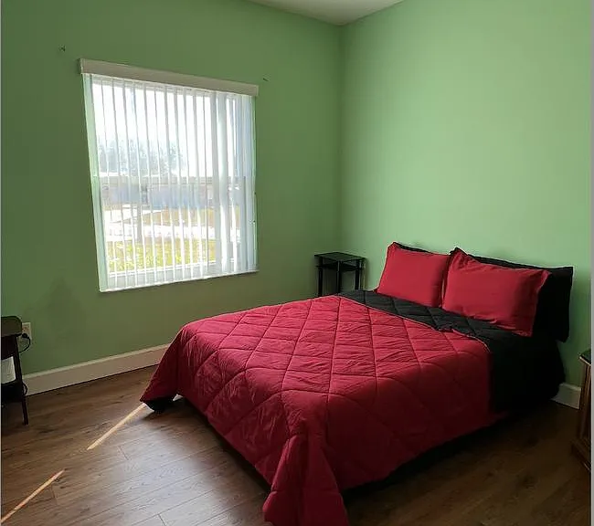 Bedroom with wood-style flooring, a ceiling fan, and a large window with vertical blinds for natural light.