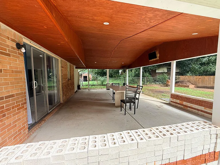 Covered backyard patio with a large concrete slab, ceiling lighting, and space for outdoor dining and entertaining.