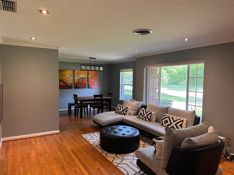 An expansive, open-concept main living area flows seamlessly into the dedicated dining space, tied together by original hardwood flooring, modern recessed lighting, and large windows that fill the home with natural light. Room