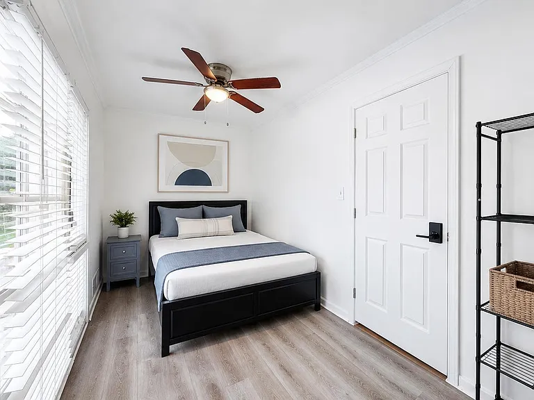 Well-sized bedroom with a large window, ceiling fan, bedside table, and shelving for convenient storage and organization.