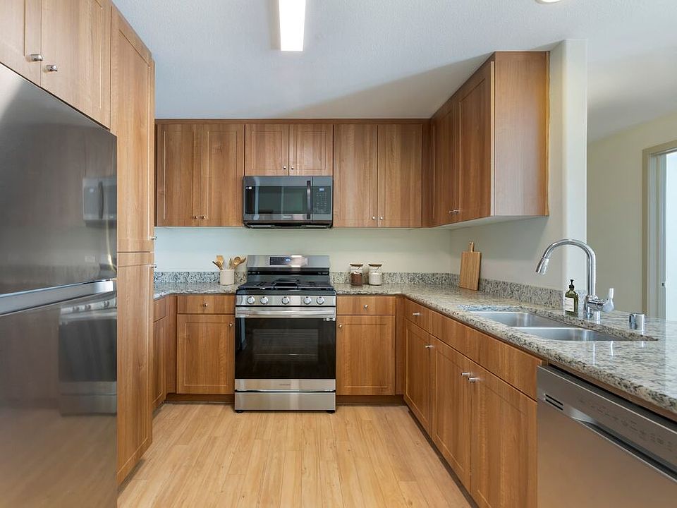 Renovated Package I kitchen with oak cabinetry, beige speckled granite countertops, stainless steel appliances, and hard surface flooring
