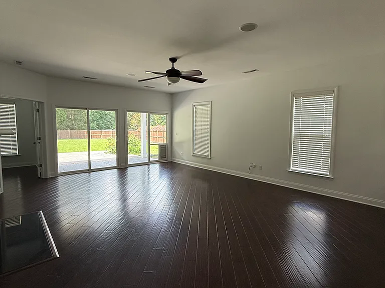 Massive living room with gleaming hardwood floors and extensive sliding doors showcasing the huge backyard lot."