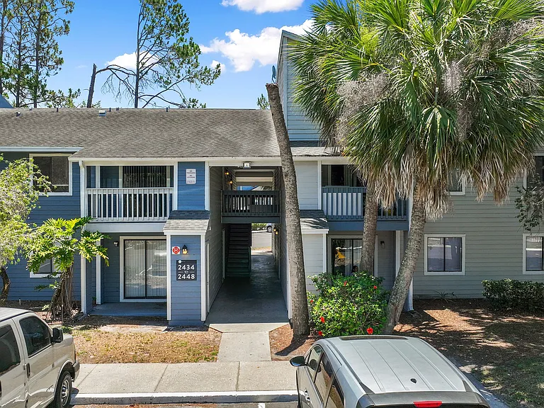 Charming apartment exterior with lush palm trees, ample parking, and welcoming ambiance in a serene setting.