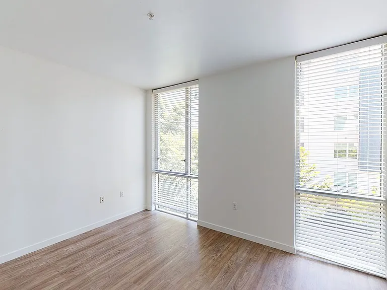 Spacious apartment bedroom with wood-style flooring and floor-to-ceiling windows.
