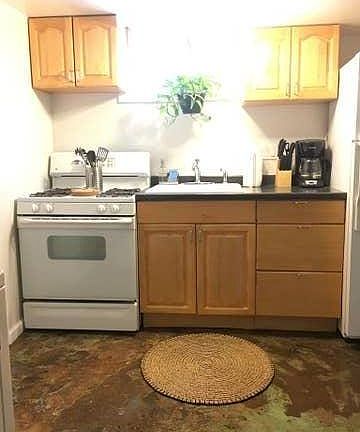 Kitchenette with stove, sink and garbage disposal, refrigerator, cabinets and open shelving for storage.