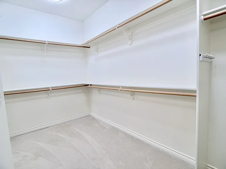 Continued view of the expansive walk-in closet, showcasing additional custom shelving and generous hanging space.